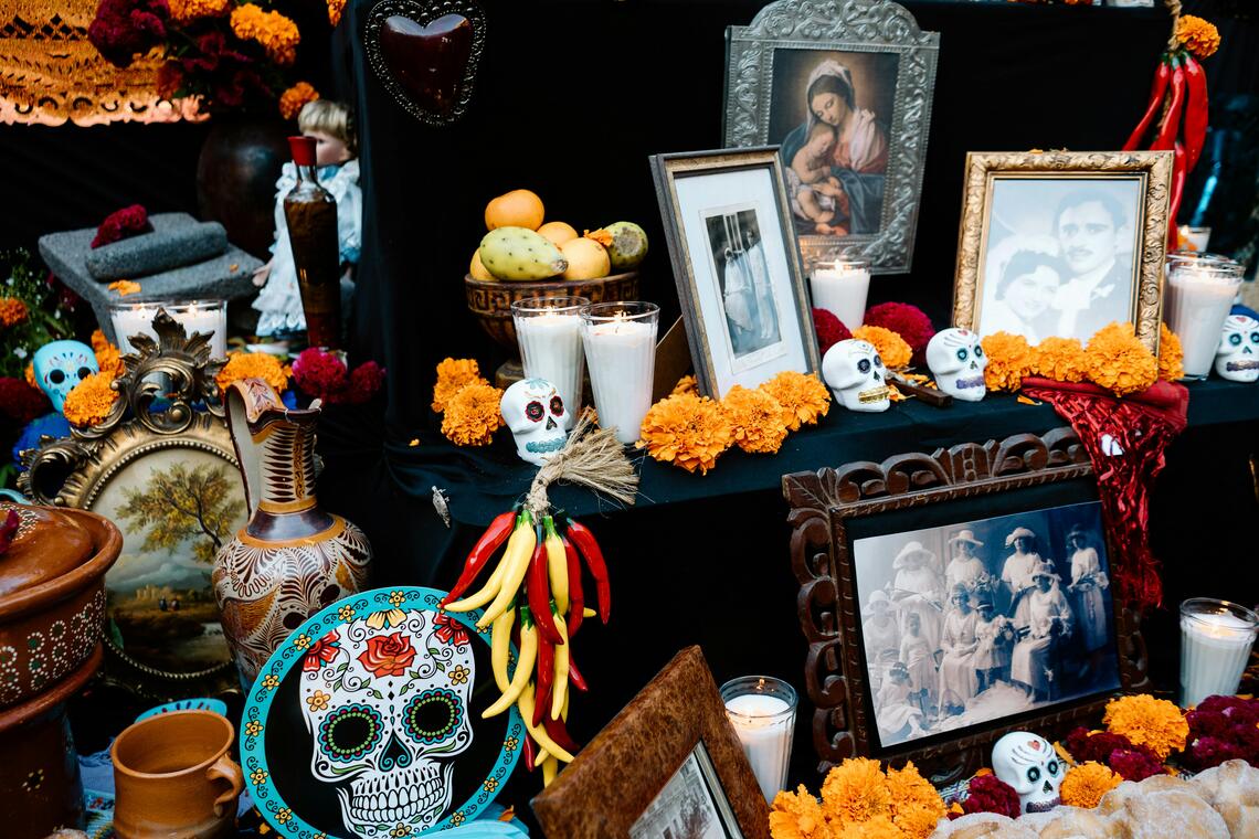 Photo of a Dia De Muertos altar with family photos, Mexican skull art, candles, flowers.