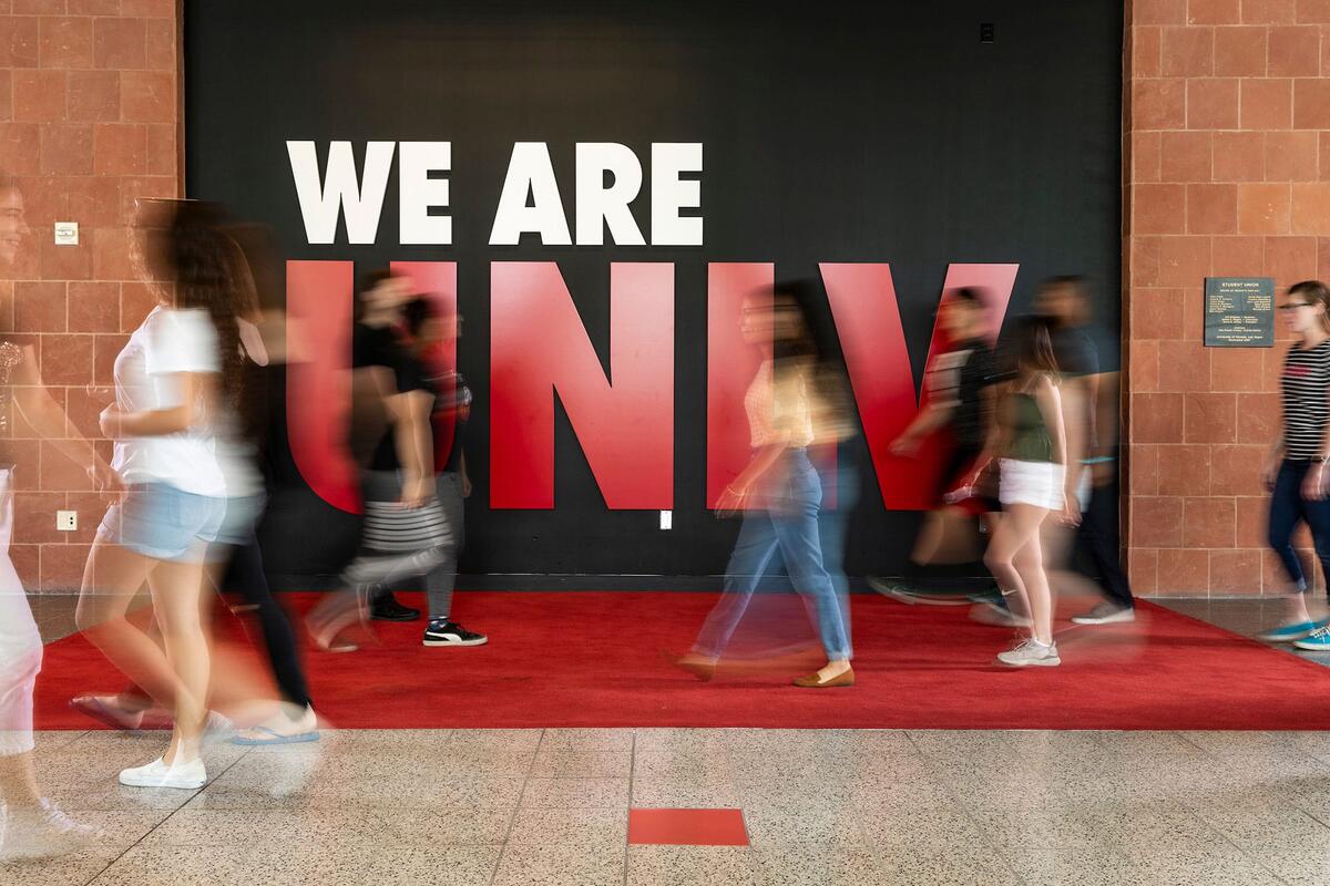 Students blurred as they walk by We Are U-N-L-V sign