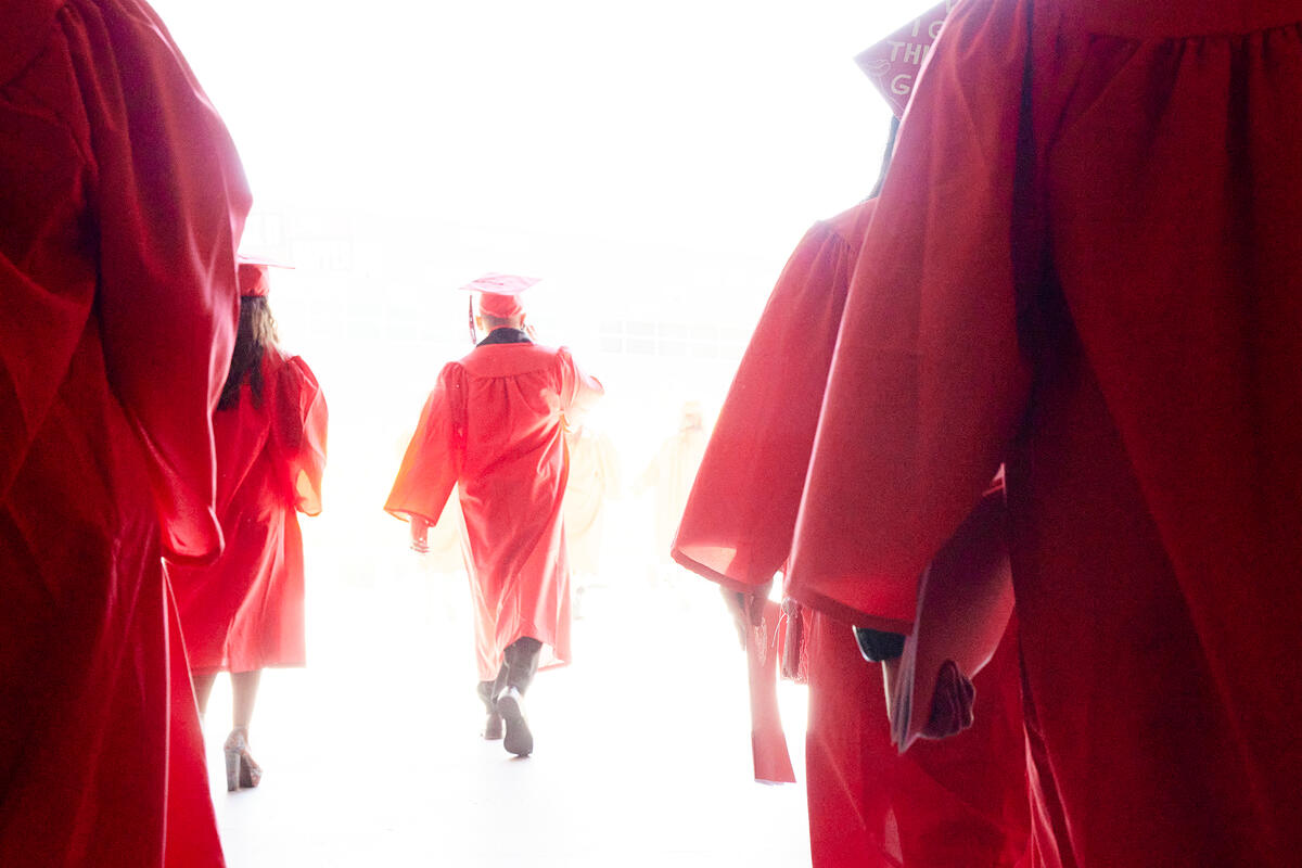 Students in cap and gown walking toward light