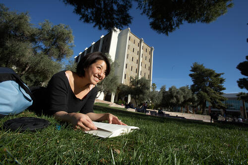 Student laid out on the grass and reading a book