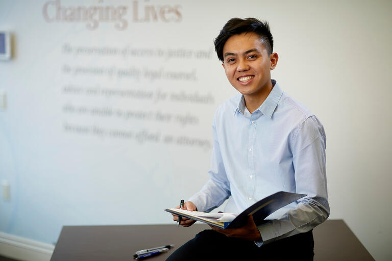 A student with notes in front of class holding a binder with a projection on the wall that says Changing Lives.