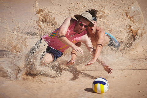 Two men dives for ball in the water.